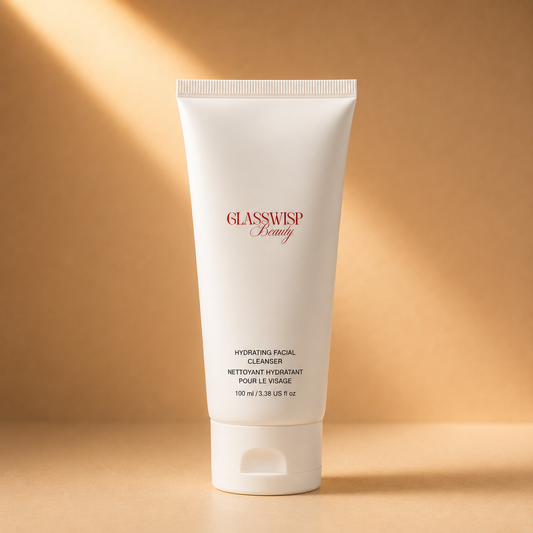 A white squeeze tube of GLASSWISP Beauty Hydrating Facial Cleanser, standing upright on a warm beige surface with soft diagonal sunlight and shadows.